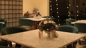 Comedor de hotel con una mesa de mármol, sillas verdes y un centro de mesa floral.