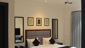 Una habitación de hotel moderna con una cama grande, una mesita redonda pequeña, un sillón azul y un ventilador de techo.