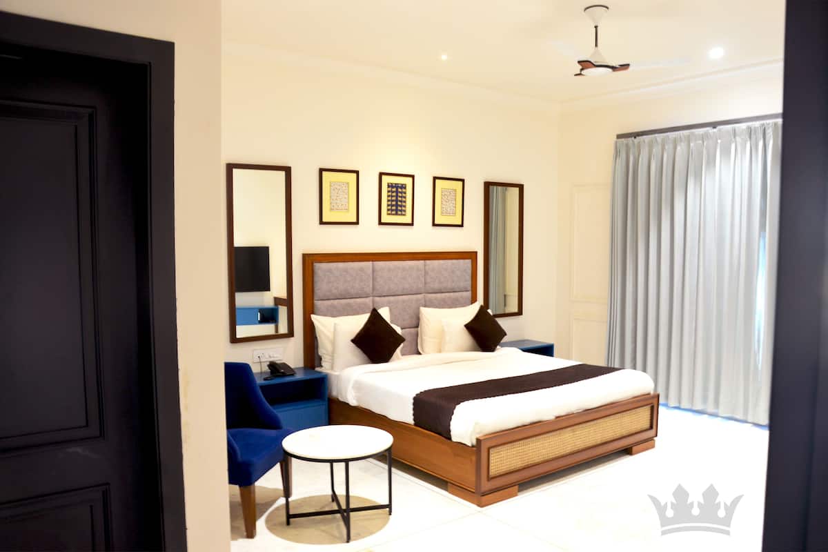 Een moderne hotelkamer met een groot bed, een klein rond tafeltje, een blauwe fauteuil en een groot raam met gordijnen.
