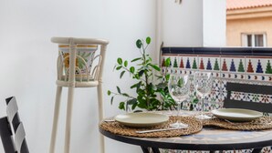 Una mesa dispuesta con platos y copas de vino, una silla de mimbre y una planta en maceta.