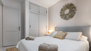 Una cama bien hecha con toallas dobladas, un espejo decorativo en la pared y una puerta cerrada.