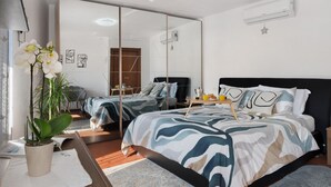 Une chambre moderne avec un grand miroir, un lit avec une literie à motifs, une table de chevet et une plante en pot.