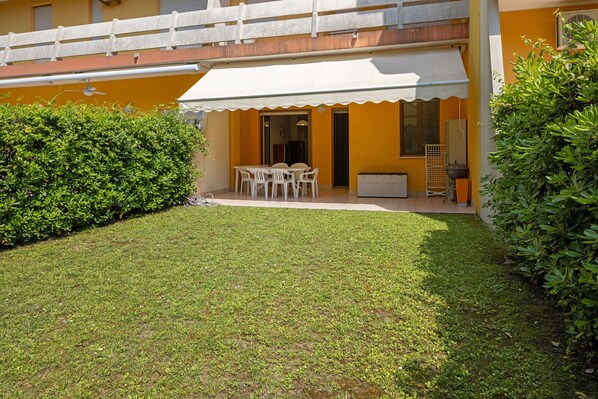 A building with a white awning, a patio with a table and chairs, and a well-maintained lawn.