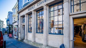 A building with a sign reading "SEASALT CORNWALL" and a storefront with clothing items on display.