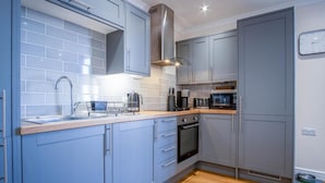 A modern kitchen with grey cabinets, a stainless steel range hood, a built-in oven, and a microwave.