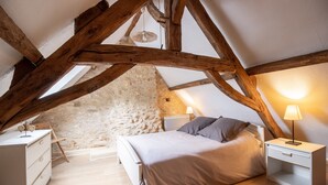 Ett sovrum med ett tak i loftstil, en vägg av sten, synliga träbjälkar, en säng, sängbord och en hängande lampa.