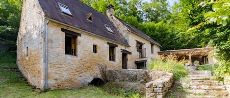 A stone building with a sloped roof, a small window, and a stone staircase leading to a covered area.