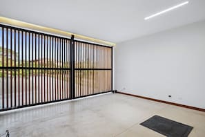 Una habitación con un gran ventanal corredera, piso de baldosas y vistas al exterior.