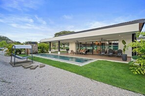 Una casa moderna con piscina, mobiliario de exterior y un patio cubierto.