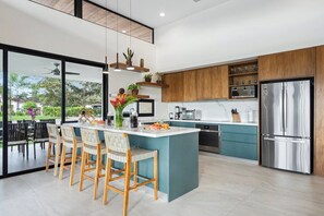 Una cocina moderna con una isla central, armarios de madera y electrodomésticos de acero inoxidable, con vistas al exterior.