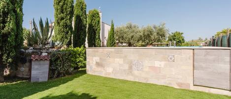 A well-maintained garden with a stone wall, tall trees, and a clear blue sky.