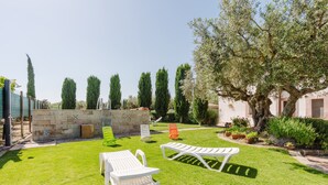 Un espacio exterior bien cuidado con un muro de piedra, diversas opciones de asientos y un árbol grande que proporciona sombra.
