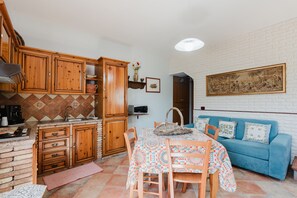 Une cuisine de taille réduite avec des meubles en bois, une table à manger avec des chaises, un canapé bleu et une œuvre d’art suspendue au mur.