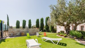 Un jardín bien cuidado con un muro de piedra, varias sillas de descanso y una variedad de árboles.