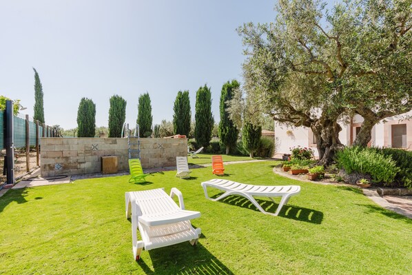 Un jardin bien entretenu, agrémenté d’un mur en pierre, de plusieurs chaises longues et de différentes espèces d’arbres.