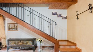 Una escalera de madera con barandilla de metal, un banco con un jarrón de flores y un suelo de baldosas.