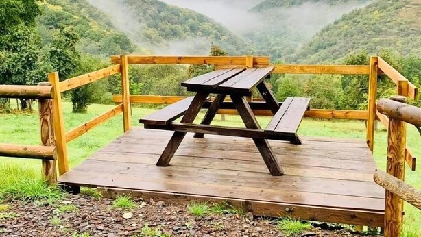 A wooden picnic table on a platform with a view of a valley and mist-covered hills.