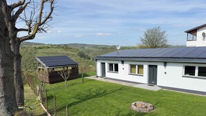 A modern house with a solar panel roof, a fenced yard, and a stone fire pit.