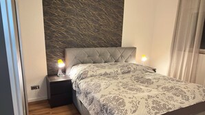 A bedroom with a tufted headboard, a patterned bedspread, bedside lamps, and a wall with a textured design.