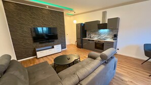 A modern living room with a flat-screen TV, grey sofa, and a small round table.