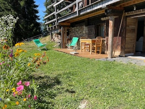 A rustic wooden building with a stone wall, a wooden deck, and outdoor seating.
