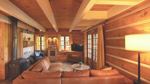 Un accogliente interno di una baita in legno, con un divano in pelle, una televisione e un caminetto.