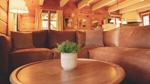 Un accogliente interno di una casetta in legno con un divano in pelle, un tavolo rotondo in legno e una pianta in vaso.