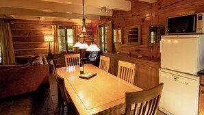 Una cucina accogliente in stile baita con pareti in legno, un tavolo da pranzo, sedie, un frigorifero e un forno a microonde.