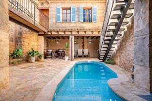 Un patio de piedra con piscina, mobiliario exterior y una escalera.