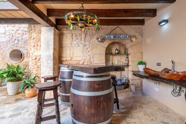 Un rústico área de bar con paredes de piedra, barriles de madera y un letrero que dice 'CAS MERCADER'.