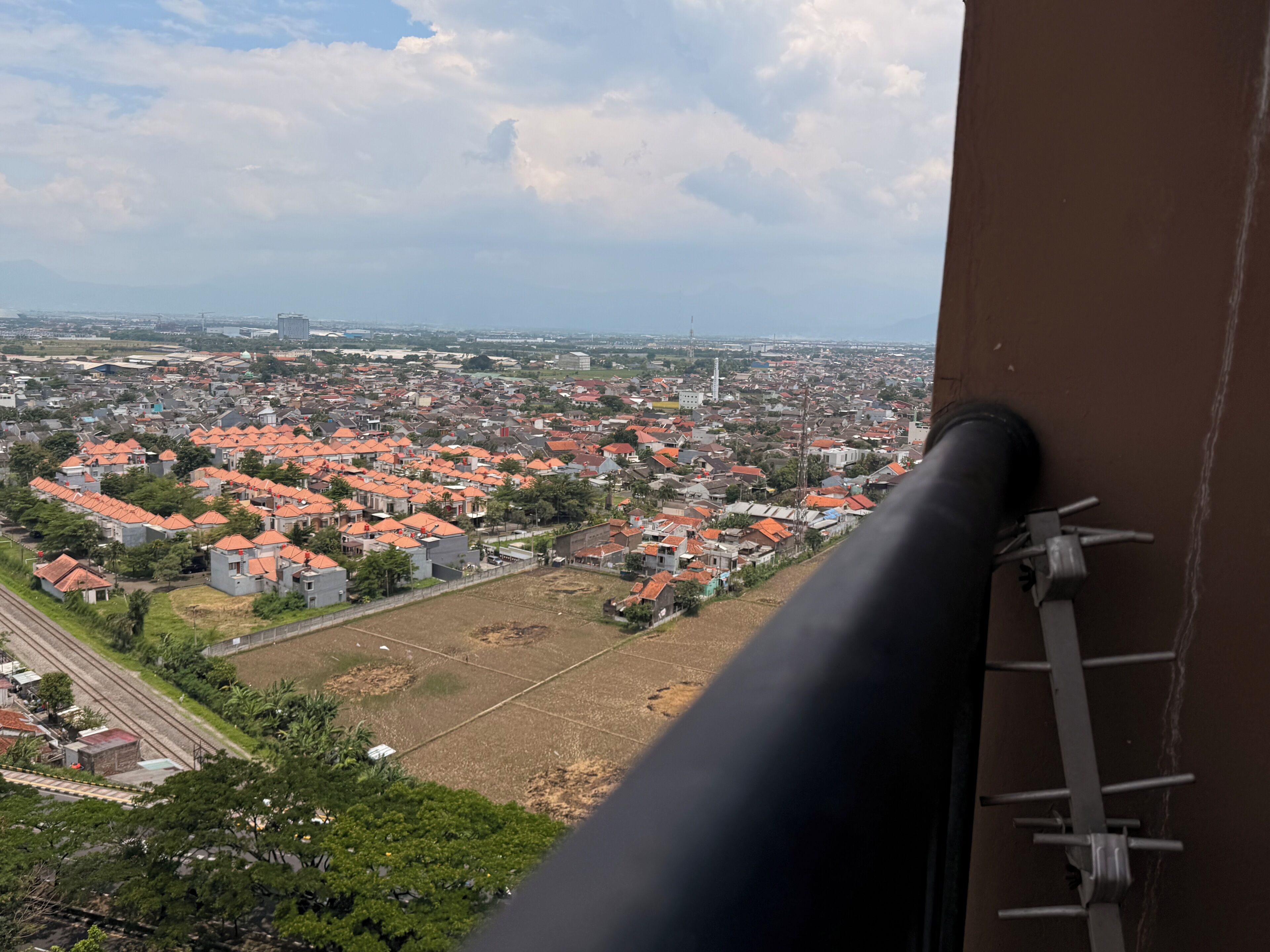 Vista panorâmica de uma paisagem urbana com edifícios de telhado vermelho, uma linha férrea e céu claro.