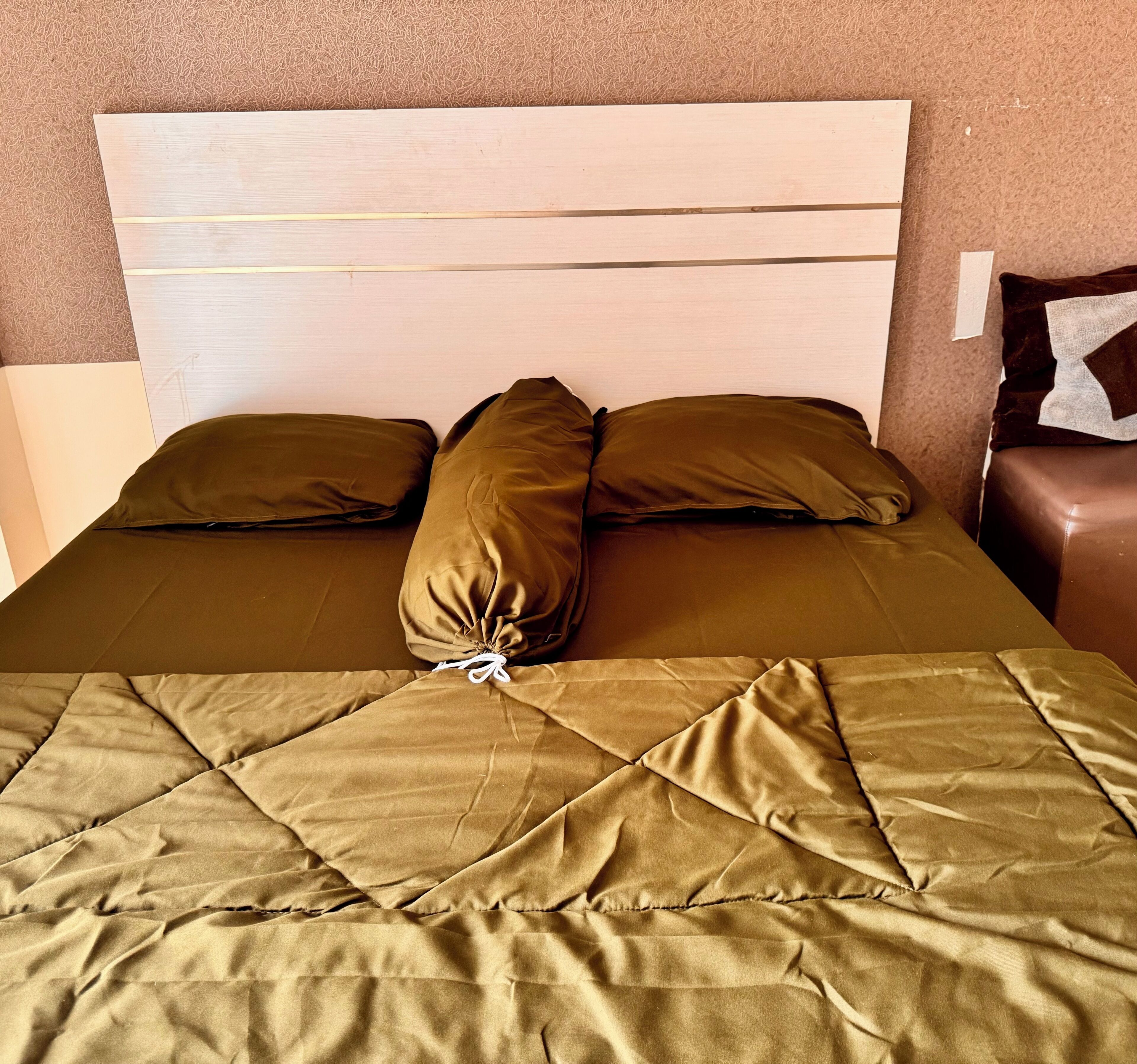 Cama bem arrumada com manta acolchoada, dois travesseiros e cabeceira de madeira.