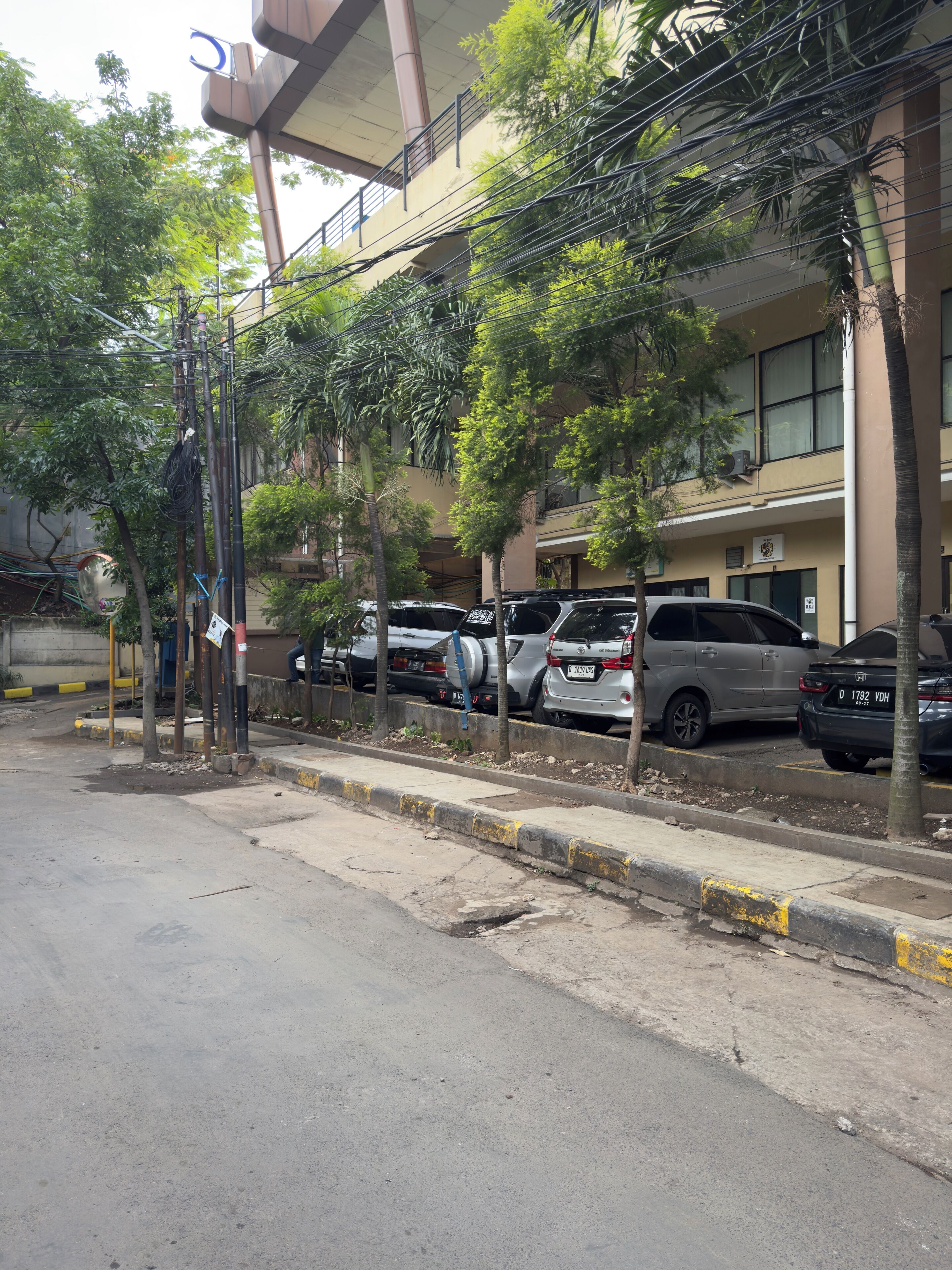 A street with parked cars, trees, and a building with a sign.