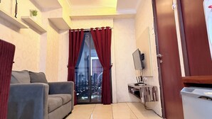 Una sala de estar con un sofá, un televisor montado en la pared, un ventanal corredero con cortinas rojas y vistas a la ciudad.