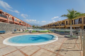 A swimming pool with a stone border, a palm tree, and a stone wall. - Vacation Apartment 'Costa Del Silencio Atlántico I' with Shared Pool, Private Terrace and Wi-Fi (Arona)