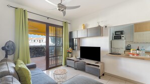 Un salón moderno con sofá, televisor y balcón con ventilador.