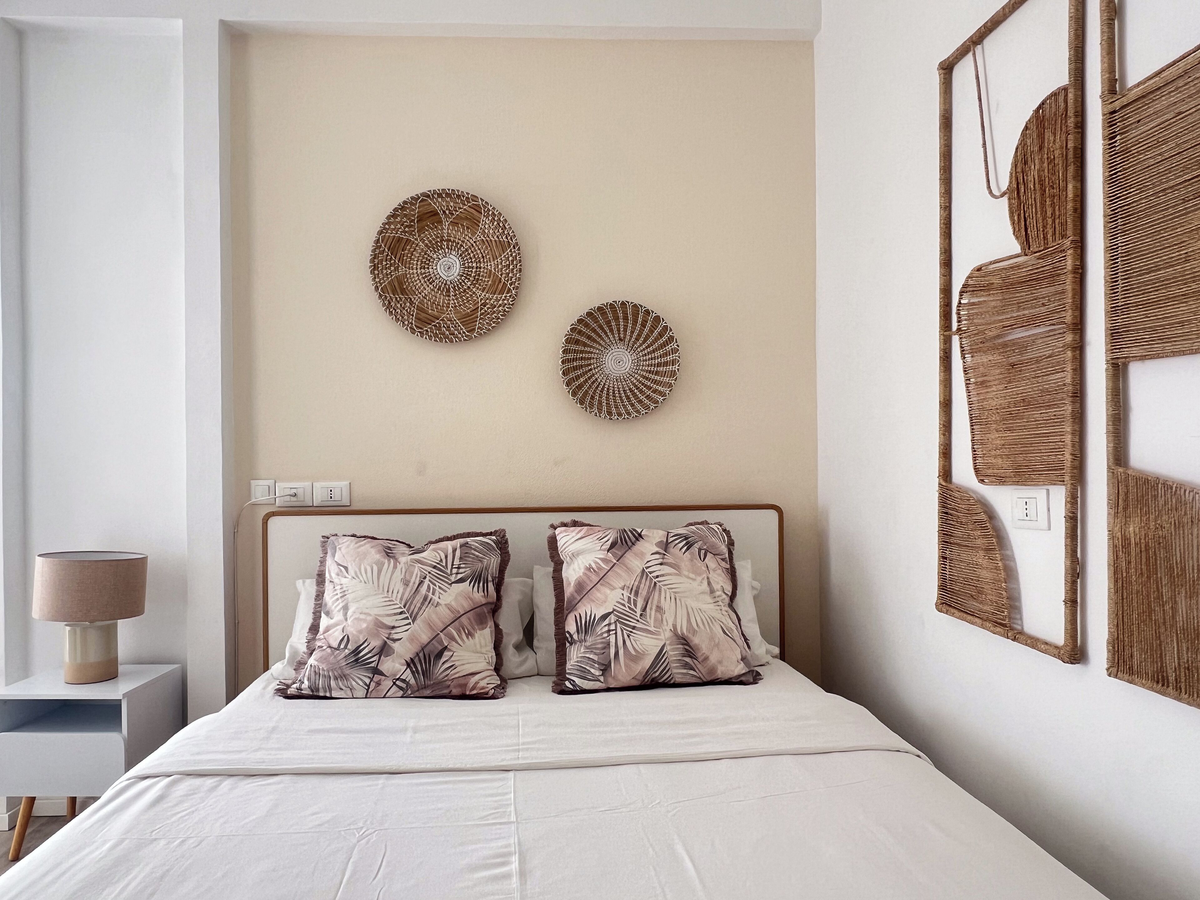A bedroom with a bed, two pillows, a bedside table, and wall decor.