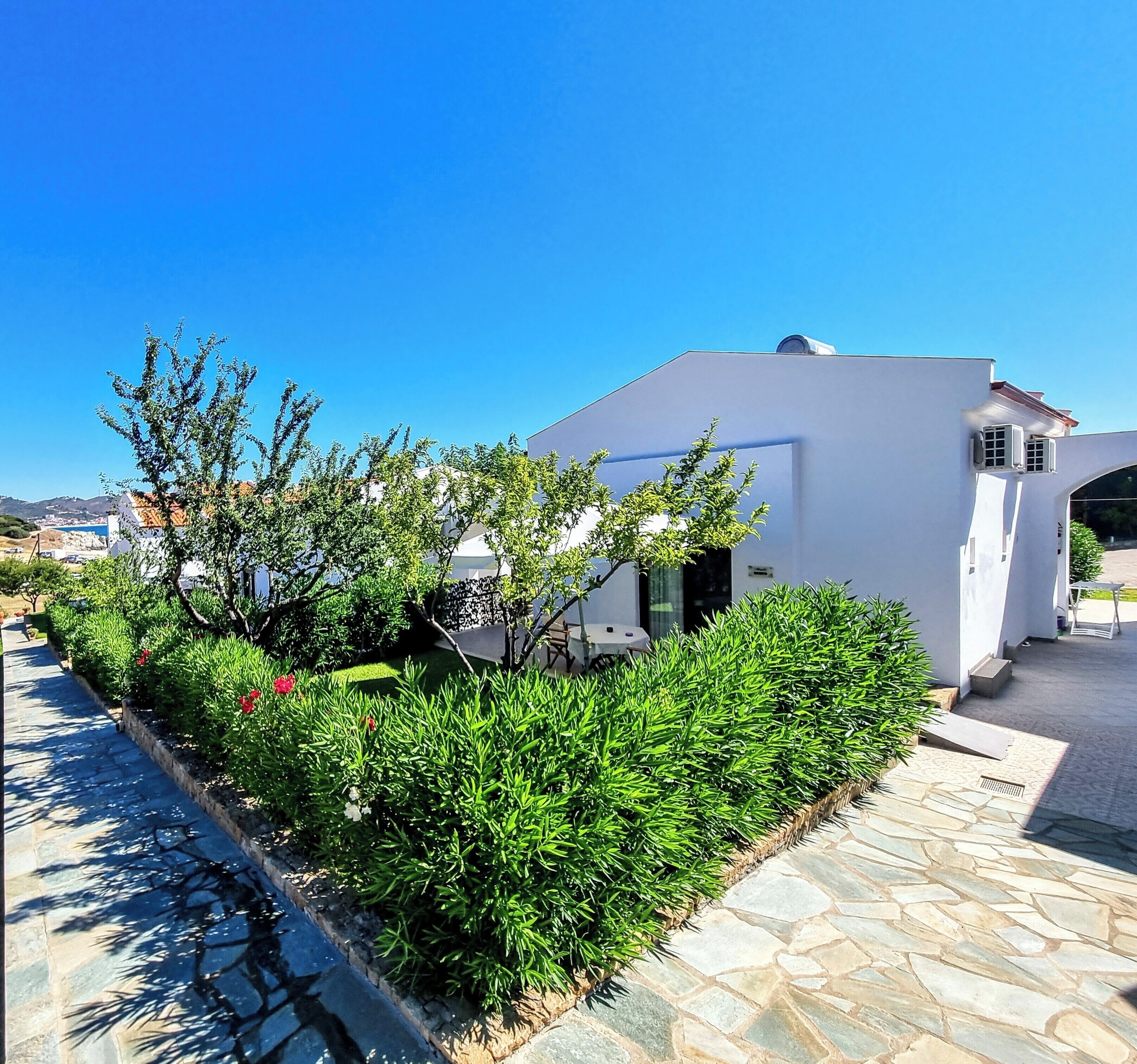 A modern building with a white exterior, surrounded by well-maintained greenery and a stone pathway.