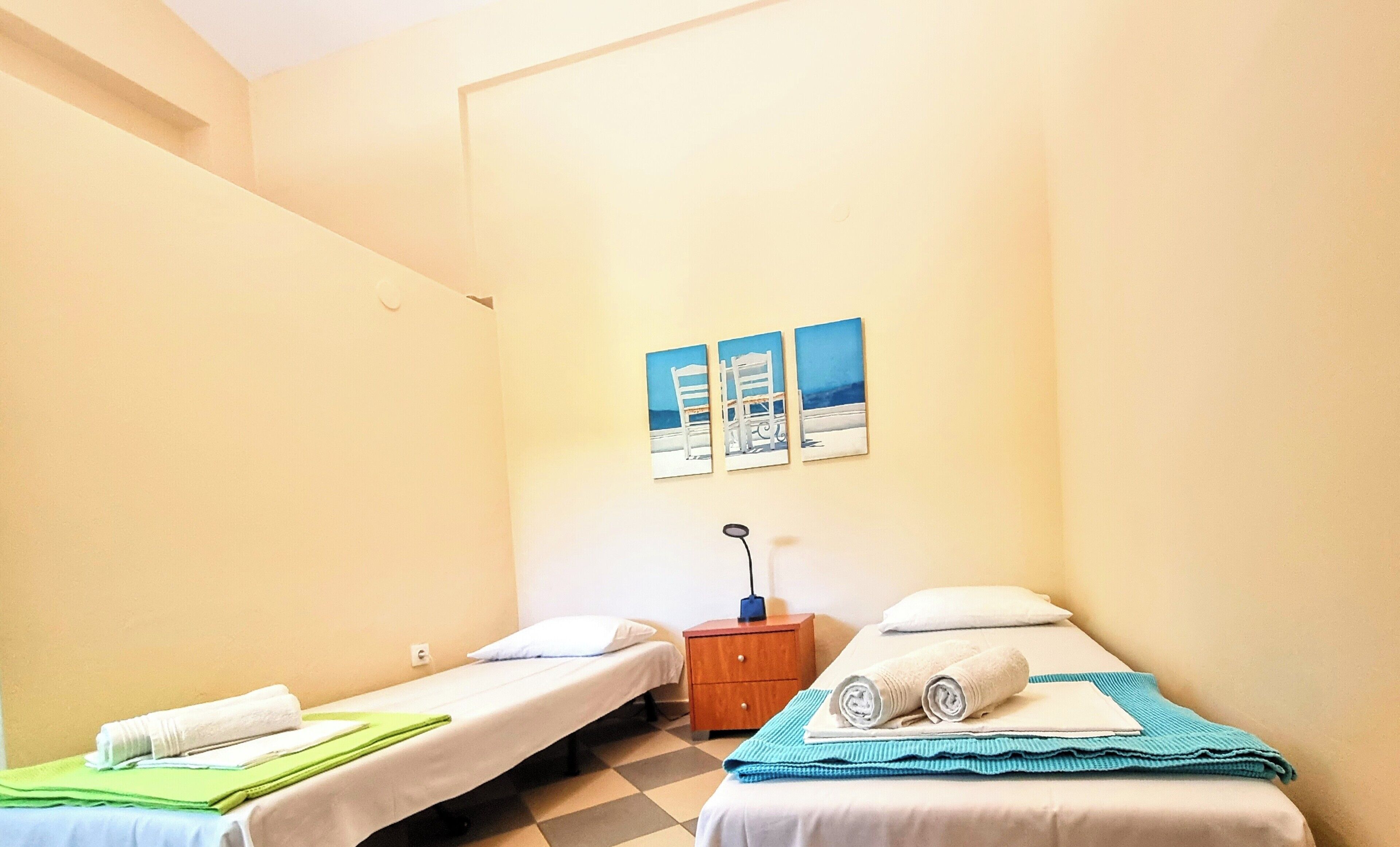 A small, clean room with two single beds, a nightstand, and a wall-mounted lamp.