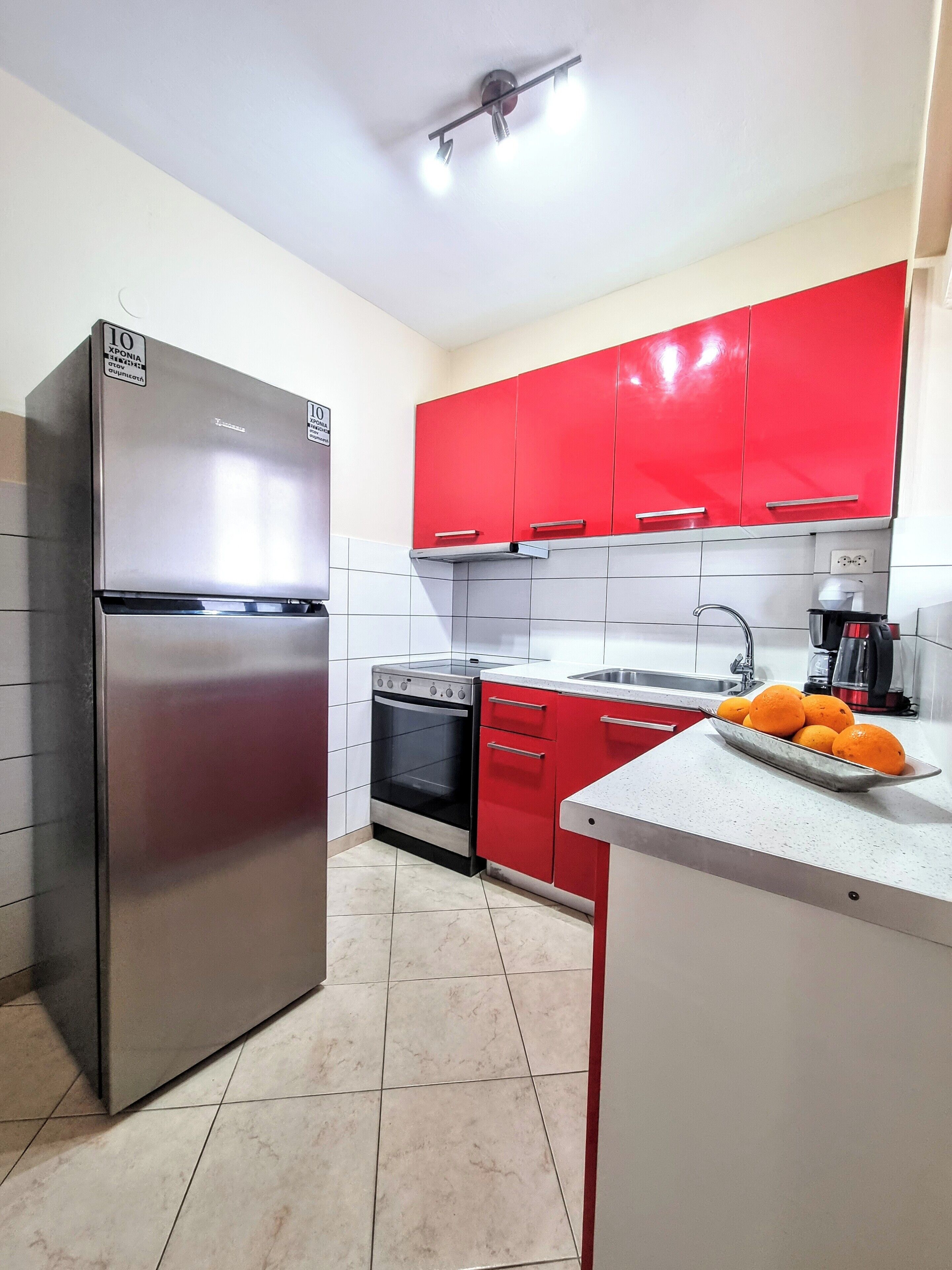 A kitchen with red cabinets, a stainless steel refrigerator, a stove, and a sink.