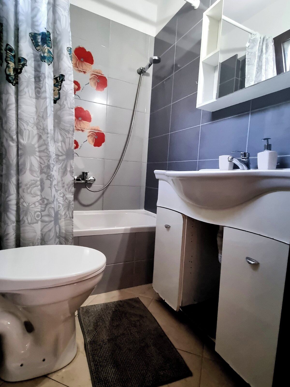 A bathroom with a toilet, a shower, a sink, and a mirror.