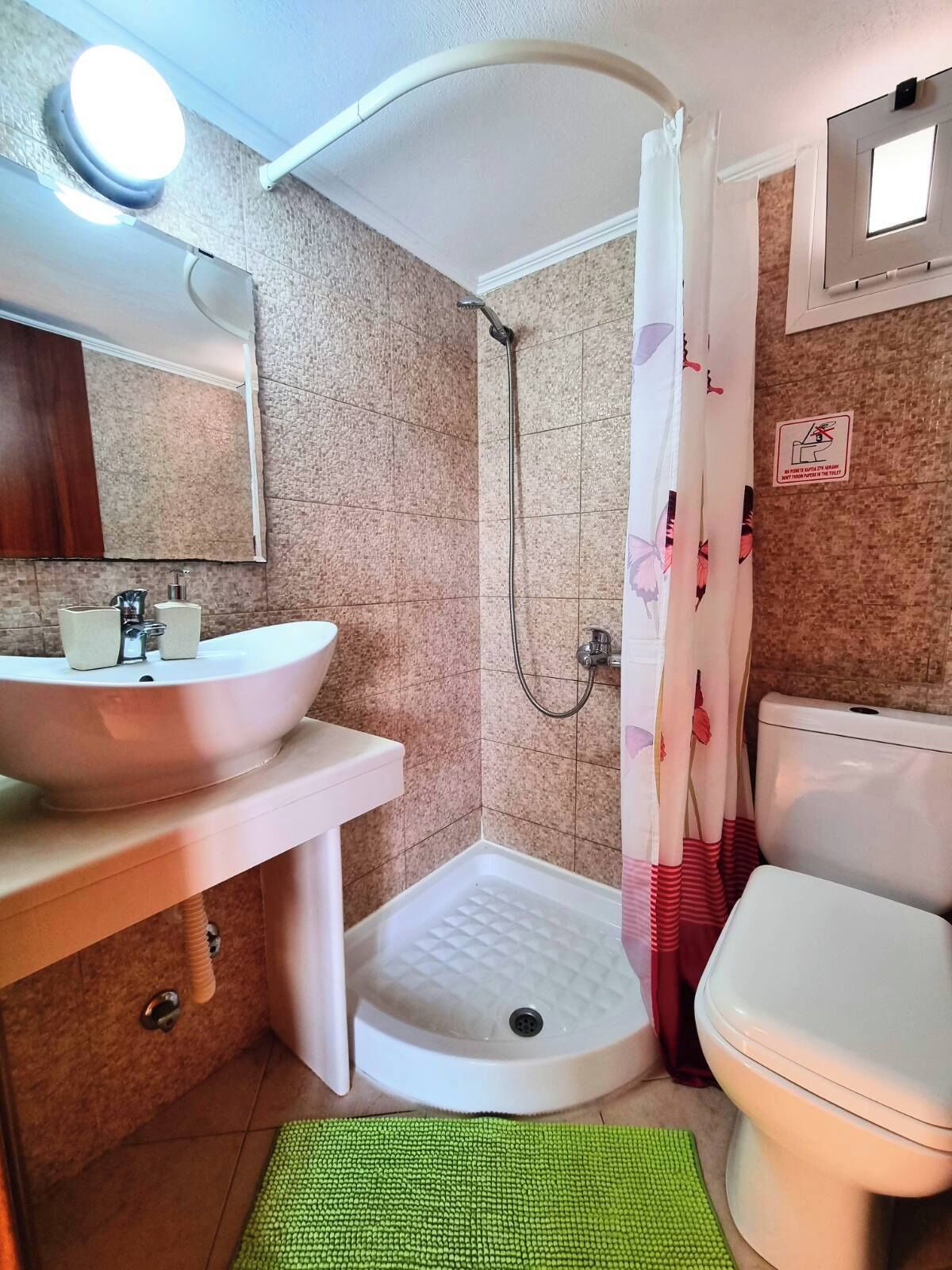 A bathroom with a sink, toilet, shower, and a green mat on the floor.