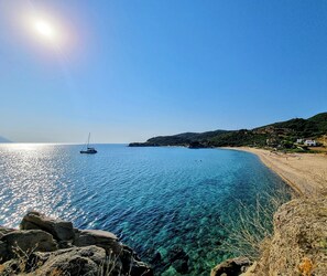 Un paysage côtier avec une eau bleue et limpide, un bateau, une côte rocheuse et un bâtiment situé sur la droite.