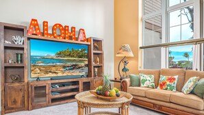 Ein Wohnzimmer mit Fernseher, Holzregalen, einem Korbtisch mit Obst und einer Couch mit floralen Kissen.