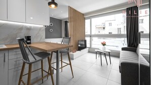A modern kitchen with a wooden dining table and chairs, a built-in oven, and a large window with a city view. - Bonsai Studios & Apartments, Nilie Hospitality MGMT (Thessaloniki)