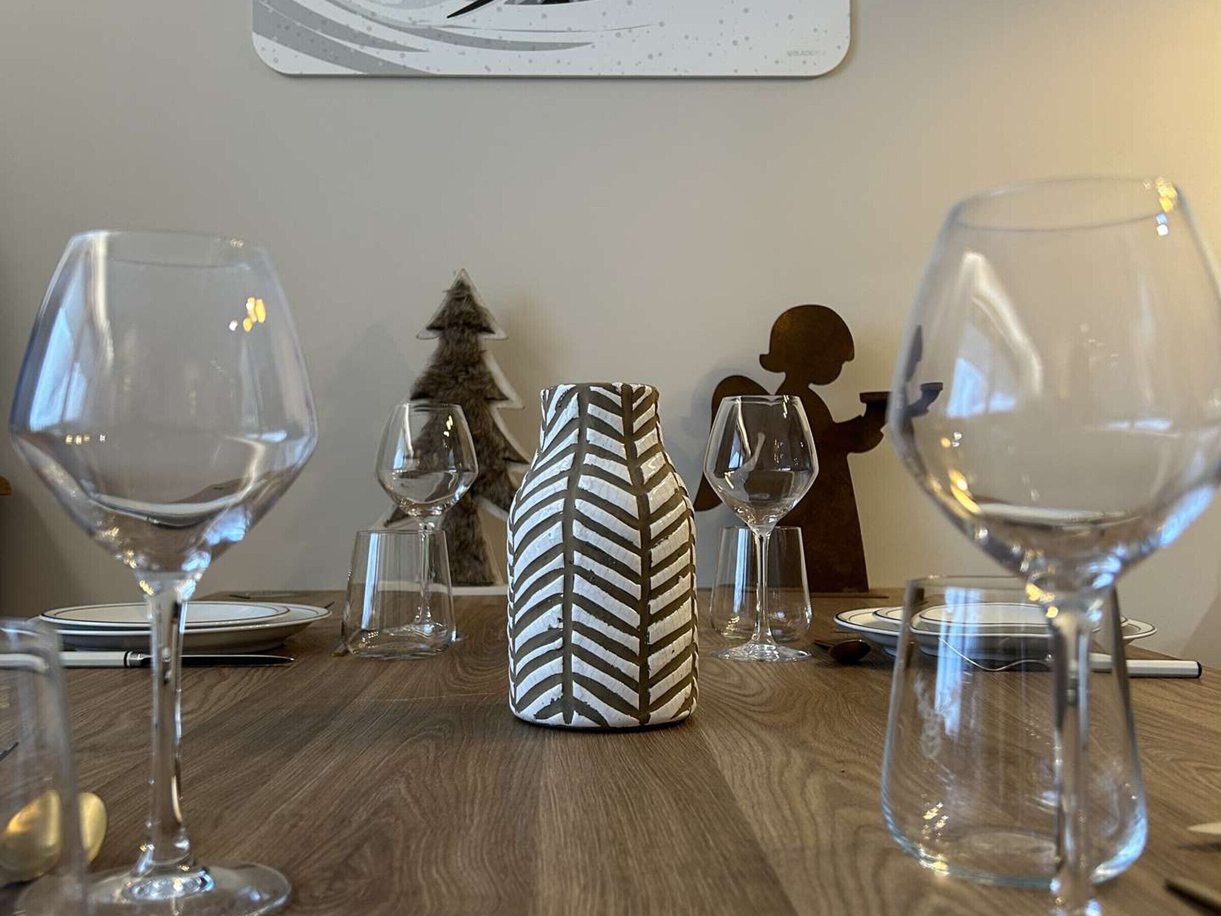 A dining table with wine glasses, a patterned vase, and a silhouette decoration.