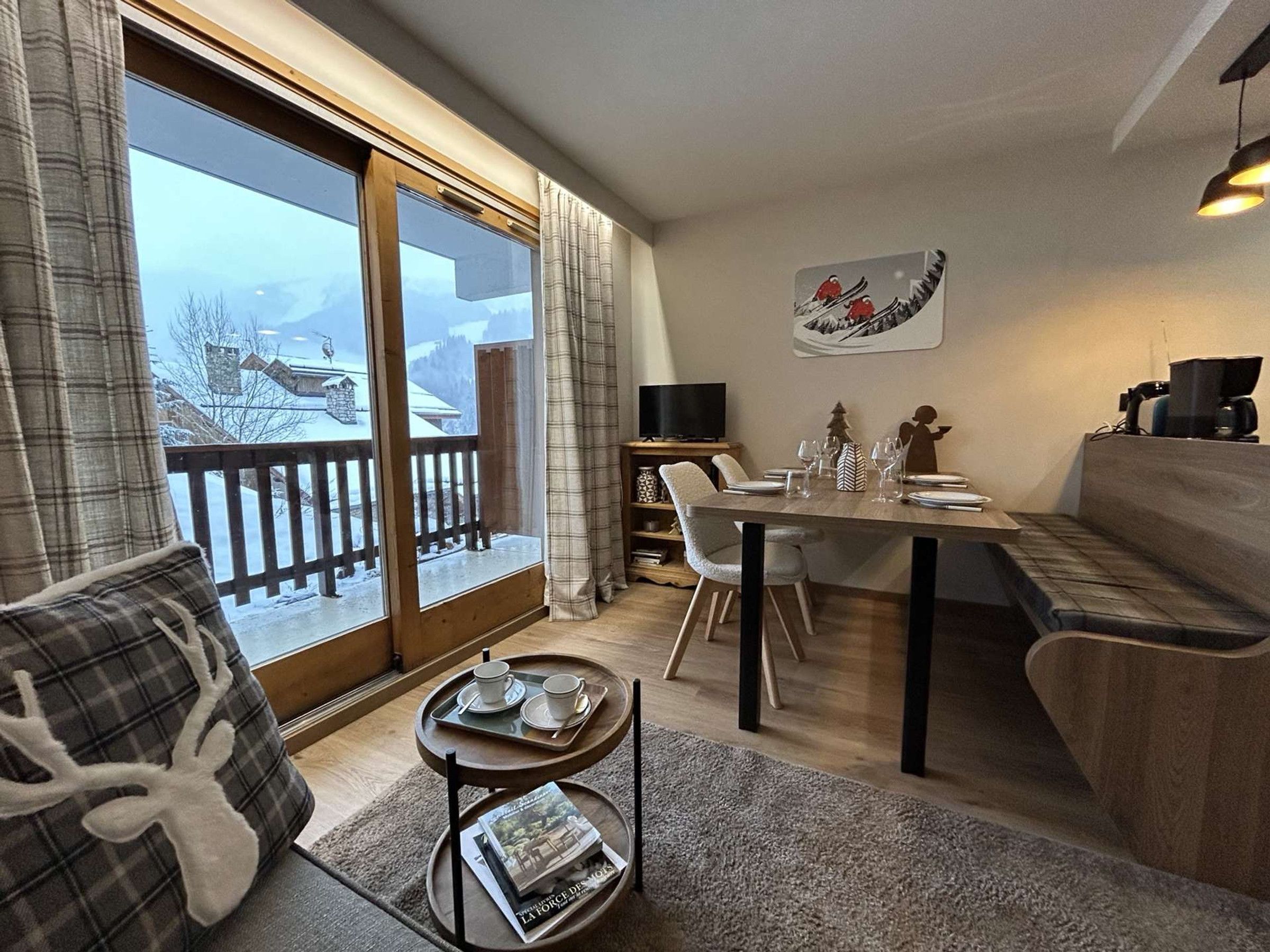 Ein gemütliches Wohnzimmer mit einem Holzespeisetisch, einer Couch und einem Balkon mit Blick auf eine verschneite Landschaft.