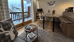 A cozy living room with a wooden dining table, a sofa, and a balcony with a view of a snowy landscape.