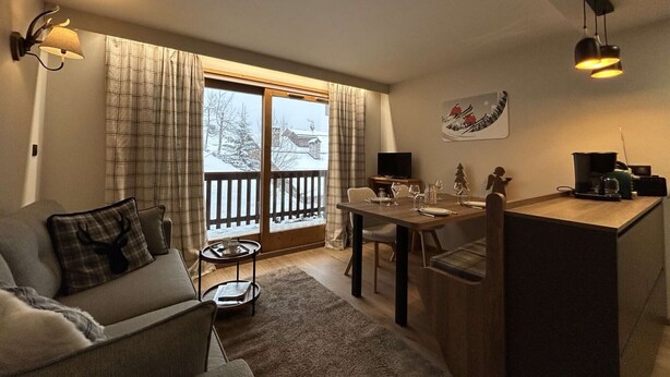 A cozy living room with a sofa, a dining table set for two, and a kitchen area with a coffee maker.