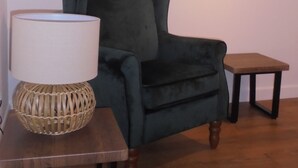 A room with a dark green armchair, a small wooden table with a lamp, and a framed picture on the wall.